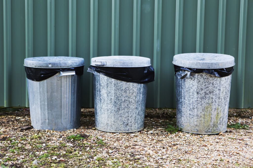 Metal Garbage Bins In A Row Against A Metal Wall