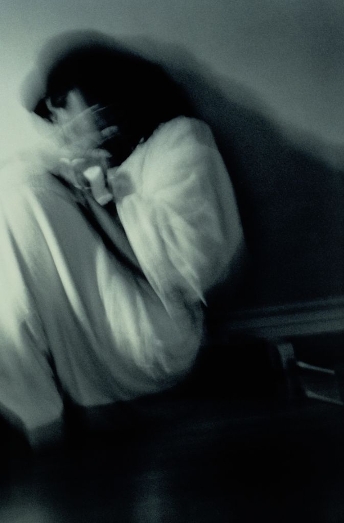 Woman curled on floor shielding herself with hands, blurred (B&W)