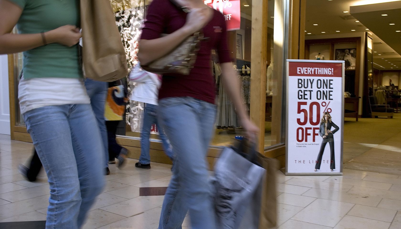 Shoppers walk past a sale sign in front
