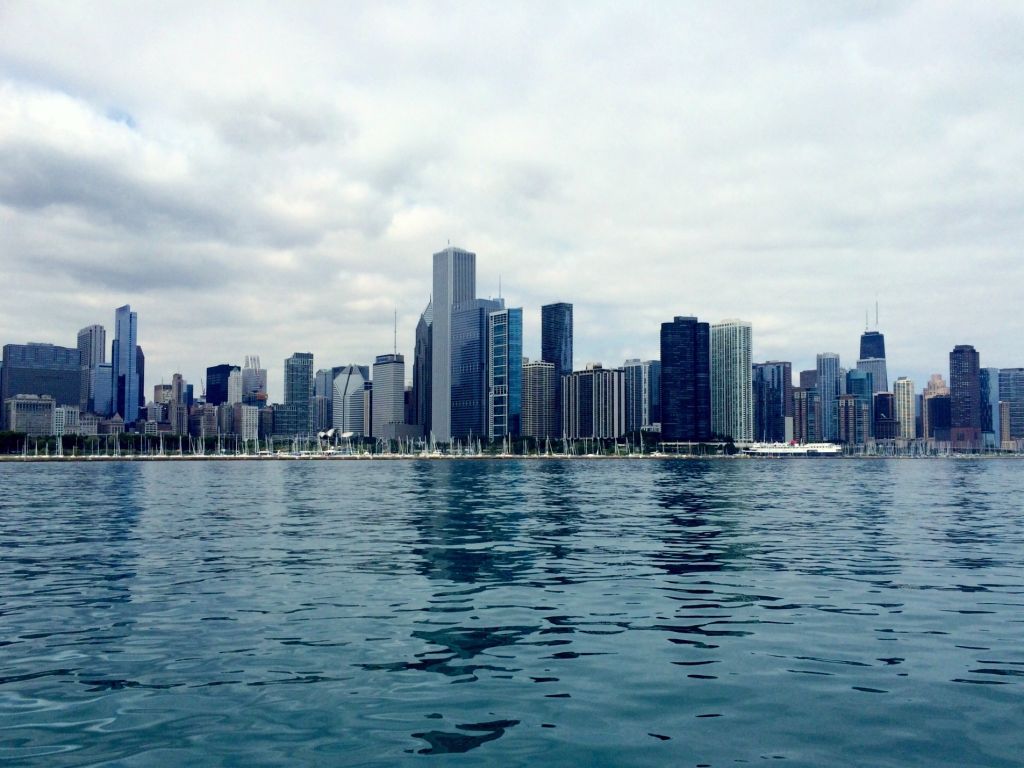 Cityscape In Front Of River Against Cloudy Sky