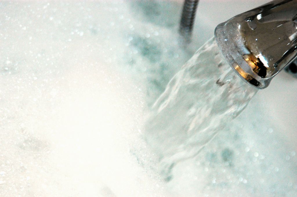 Water gushing from tap into bath containing bubble bath