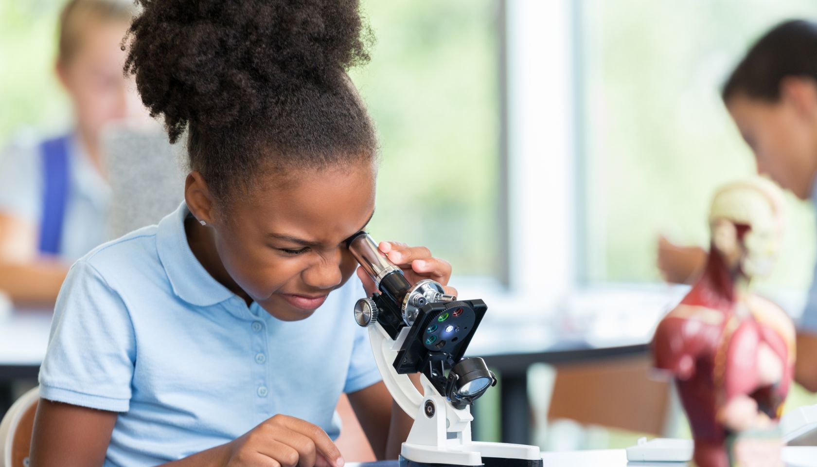 Beautiful elementary schoolgirl uses a microscope for science project
