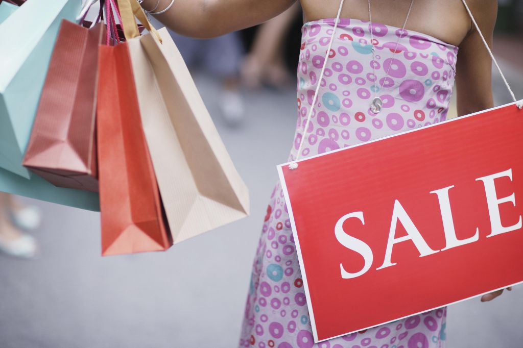 Woman outdoors holding shopping bags and wearing sale sign