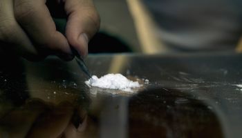 Close-up of a man's hand cutting cocaine with a blade