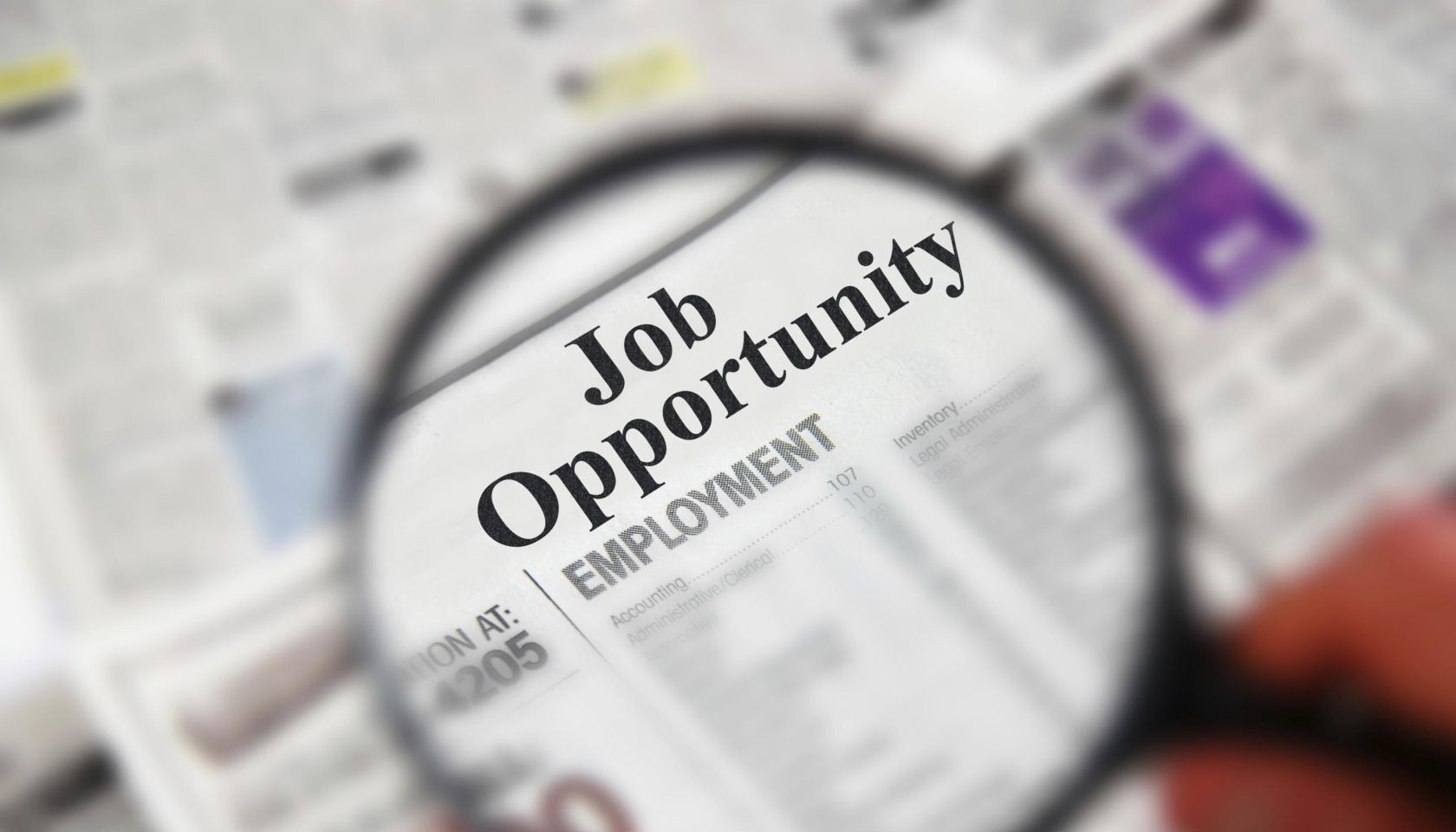 Magnifying glass over a newspaper classified section with "Job Opportunity" text