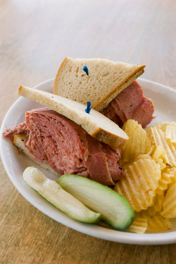 A corned beef sandwich with crisps and pickled gherkins