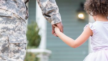 Army dad holds hands with young daughter