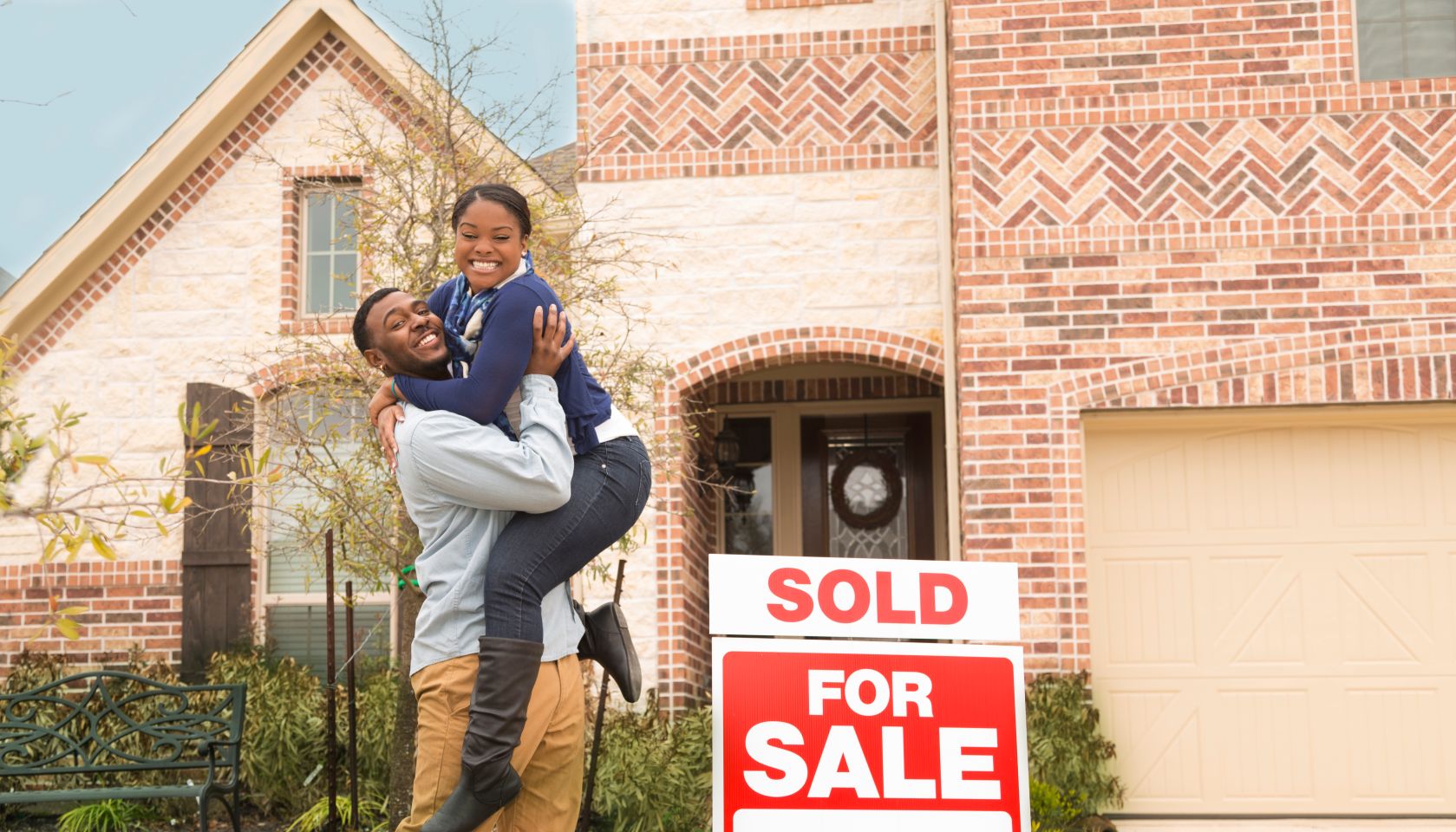 Excited couple jumps for joy in front of first home.