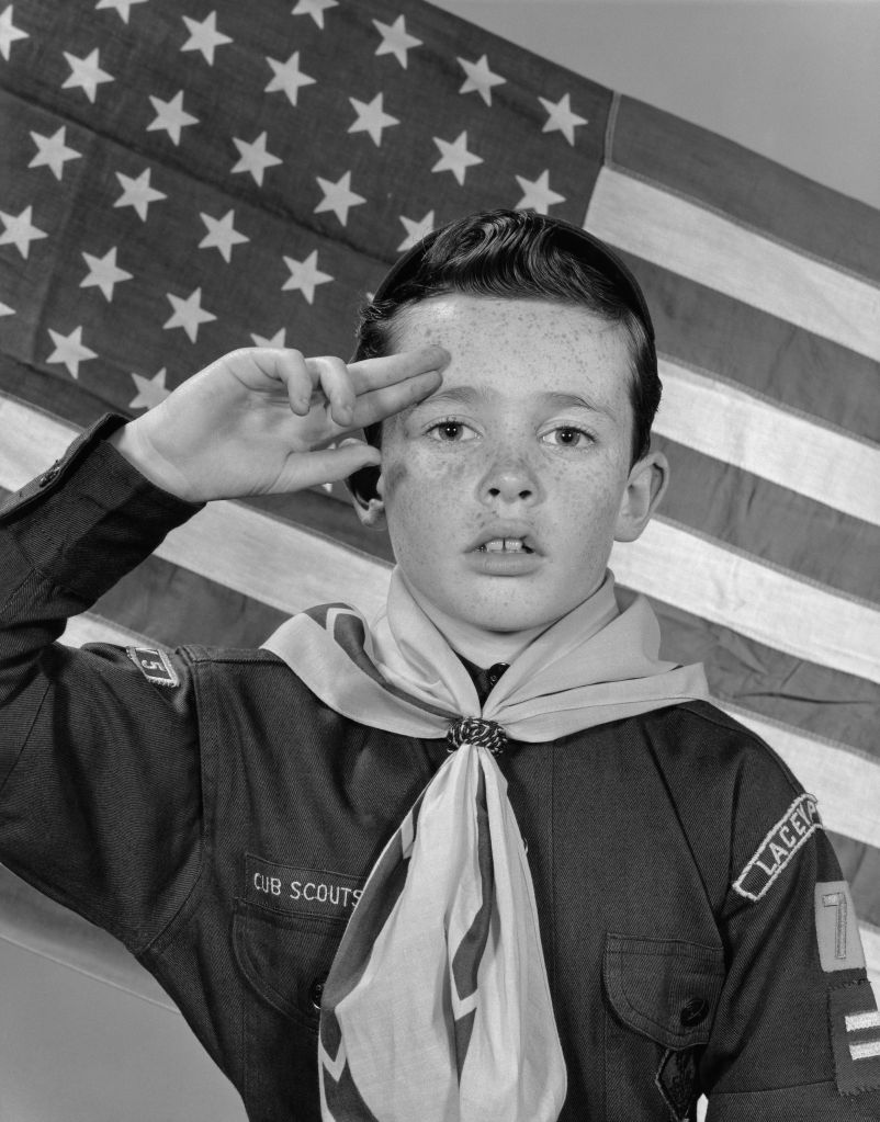 BOY SCOUT SALUTING IN FRONT OF AMERICAN FLAG