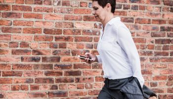 Businesswoman with briefcase and cell phone running in front of brick wall