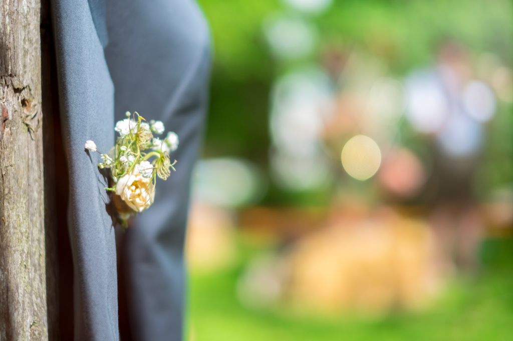 Part of a suit jacket with corsage hanging on a tree trunk.
