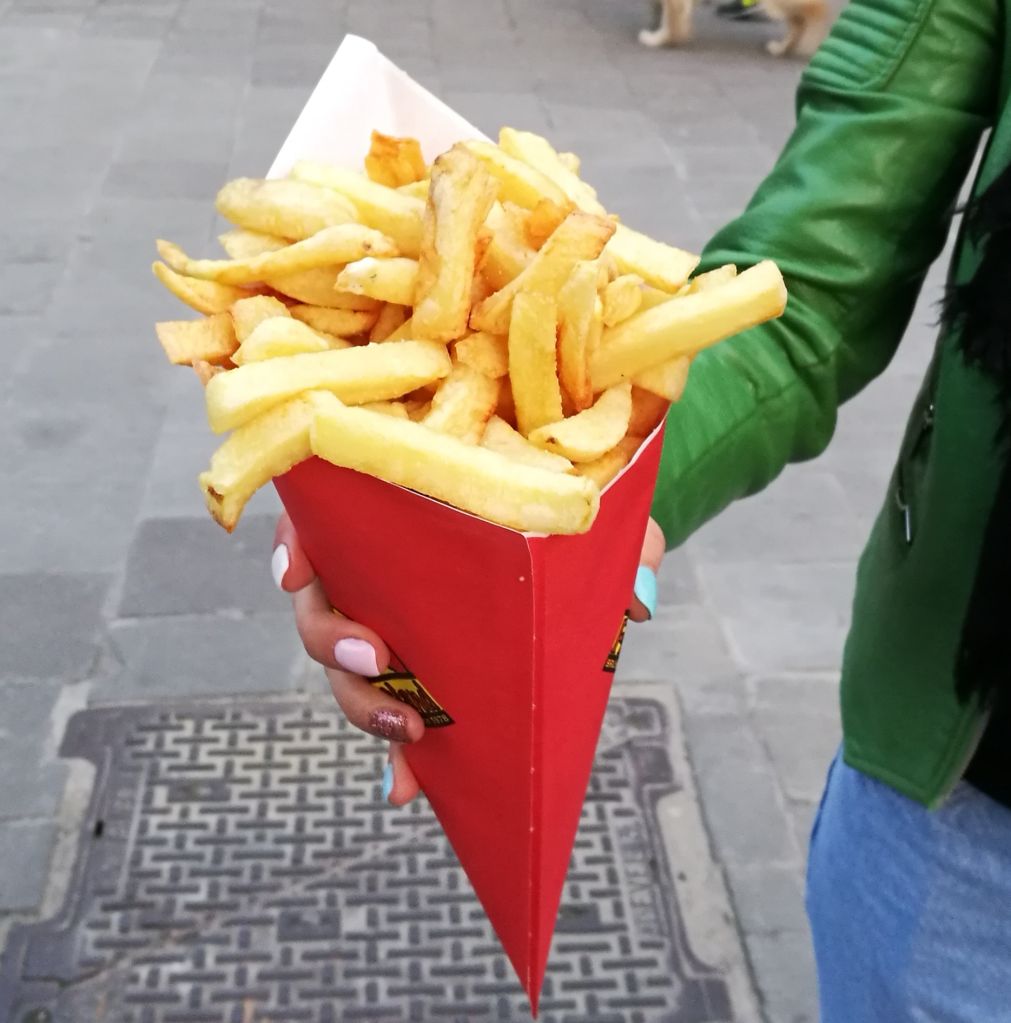 Midsection Of Woman Holding French Fries While Standing On Street