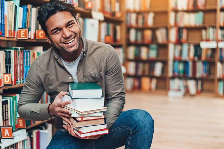 Happy young man with a pile of books in a bookstore