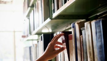 Cropped Hand Of Woman Removing Book From Bookshelf In Library