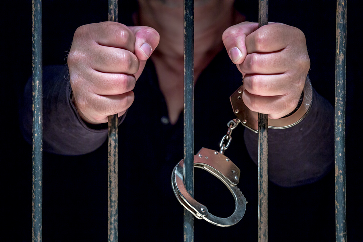 Midsection Of Prisoner Standing Behind Bars