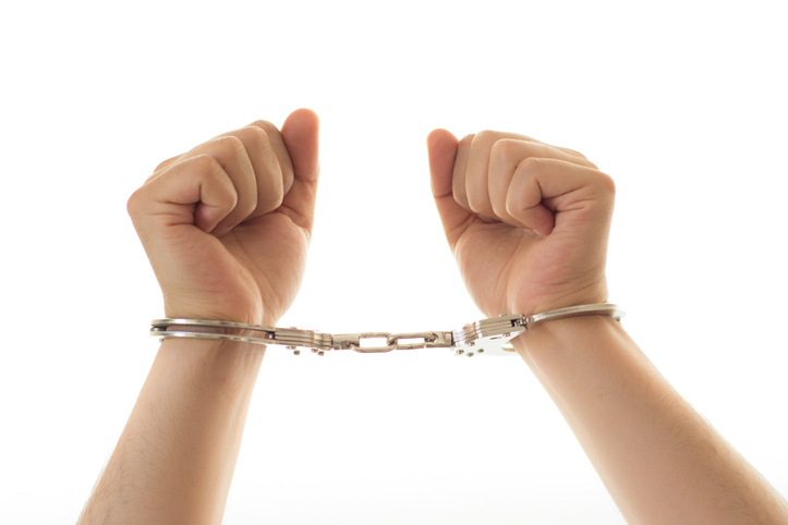 Close-Up Of Hand Wearing Handcuffs Against White Background