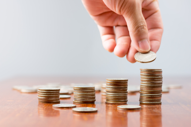 Close-Up Of Hand Stacking Coins On Table Against Wall