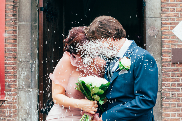 Petals Falling On Groom And Bride With Bouquet Standing Outside Building