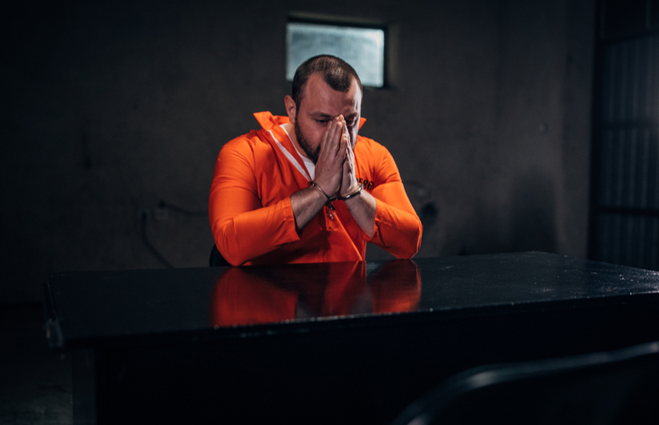 Prisoner in orange jumpsuit praying in interrogation room