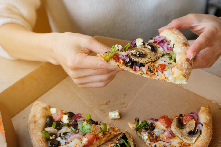 A slice of Italian Vegetable Pizza With Cheese and Mushrooms in the hands of a Girl. A Woman Takes A Slice Of Pizza And Eats It, In A Cafe Or Pizzeria. Vegetarian food. Fast food.