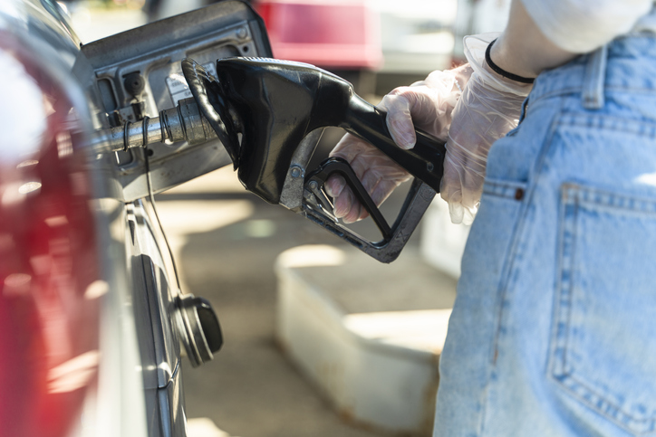 Young Caucasian White long-haired woman refueling a car at the gas station. Close-up view of her hand. She wearing protective latex gloves because of the coronavirus pandemic.