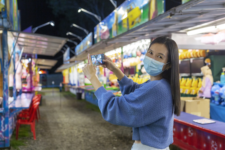 Smiling woman with face mask taking photos at amusement park