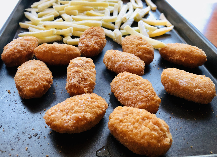 Frozen chicken nuggets and French fries on baking pan