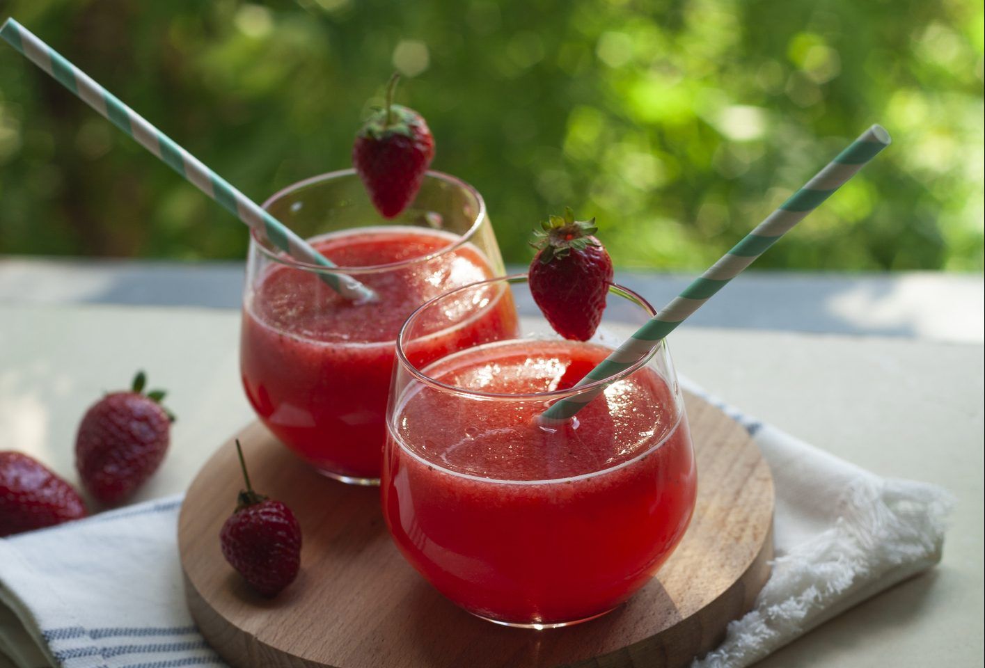 Summer drink: strawberry fruit smoothie in glasses on table over green trees background.