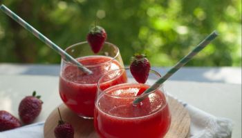 Summer drink: strawberry fruit smoothie in glasses on table over green trees background.