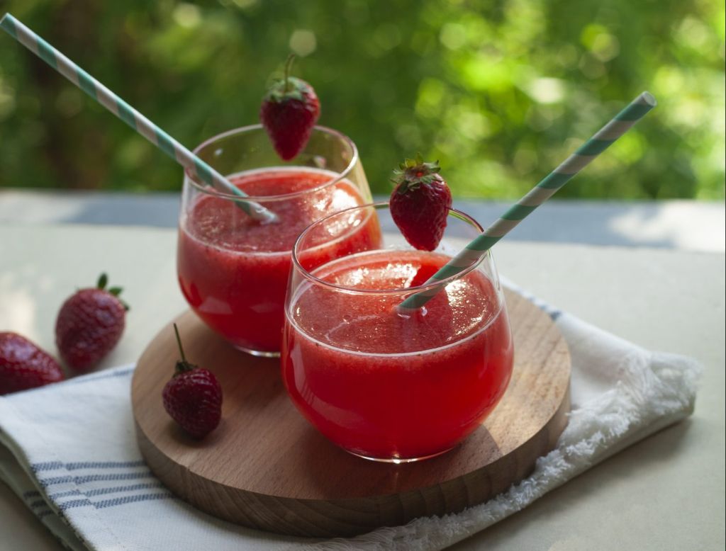 Summer drink: strawberry fruit smoothie in glasses on table over green trees background.