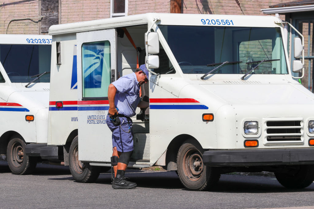 A United States Postal Service (USPS) worker exits a Grumman...