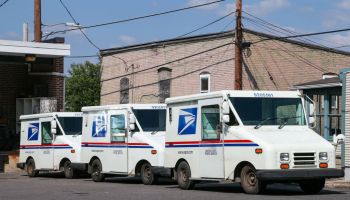 Three United States Postal Service (USPS) mail trucks are...