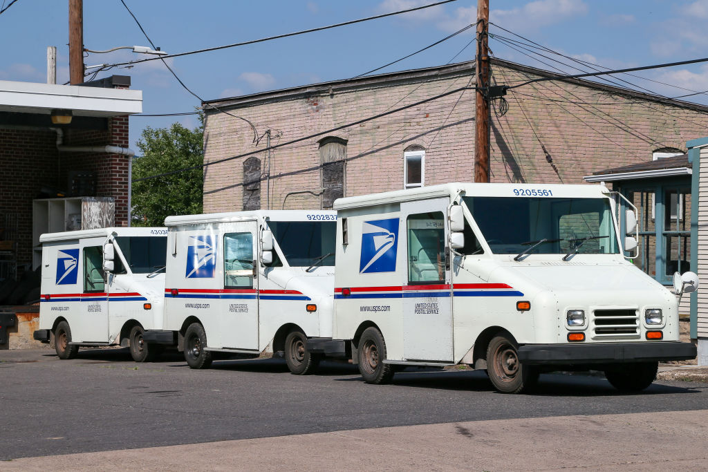 Three United States Postal Service (USPS) mail trucks are...