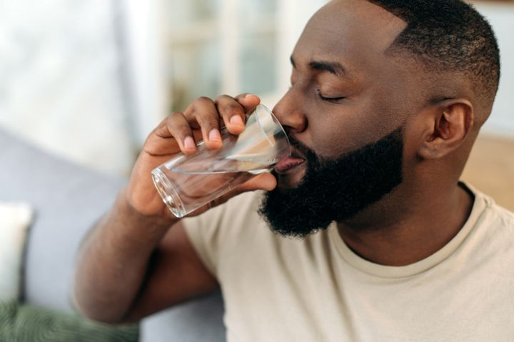 Leading a healthy lifestyle. Close-up of african american man, drinks a glass of clean water with pleasure, care his health, balances fluids in the body, replenishes energy and strength in the body