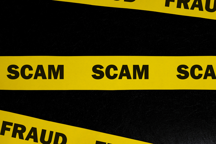 Scam and fraud alert, caution and warning concept. Yellow barricade tape with word scam in dark black background.