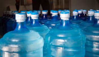A large number of plastic blue gallons of drinking water products in a drinking water plant that are arranged in a row waiting to be sold. drink water factory business concept
