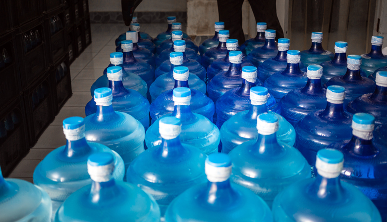 A large number of plastic blue gallons of drinking water products in a drinking water plant that are arranged in a row waiting to be sold. drink water factory business concept