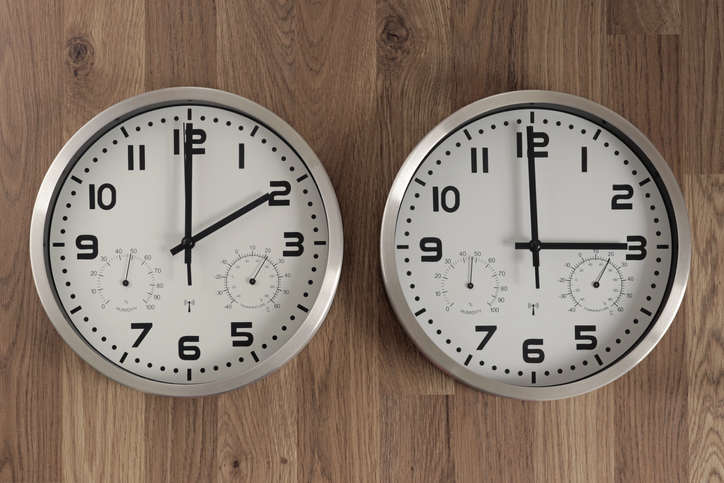 Two clocks, one showing two o'clock, the other showing three o'clock. Time change symbol.