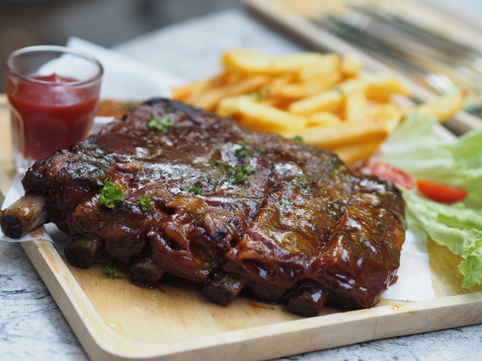 Pork Spareribs BBQ, Barbeque Pork Ribs with french fries vegetable salad, tomato sauce in a clear glass on wooden tray, food