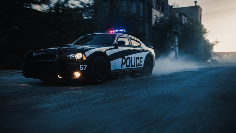 Traffic Patrol Car in Pursuit. Police Officers in Squad Car Chasing Suspect on Industrial Road, Sirens Blazing, High Speed. Cops on Emergency Response Call. Stylish Cinematic Action Packed Shot