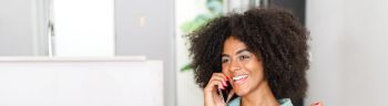 Glad to hear you. Happy excited young black woman with curly afro hair talking on the smartphone, has pleasant phone conversation