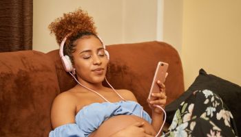 pregnant african woman lying on the sofa relaxing on the couch listening to music on headphones