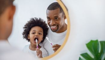 Portrait of happy family black African American father and son child boy brushing teeth in the bathroom. Morning routine with toothbrushes, fatherâs day concept