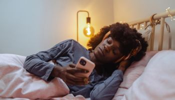 African American young woman feeling restless and using smart phone on bed at night