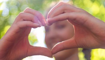 Young woman makes heart shape finger frame