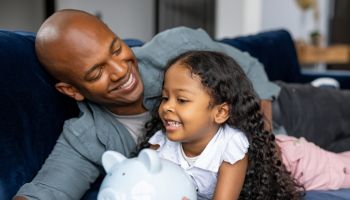Loving father teaching his daughter to save money in a piggybank