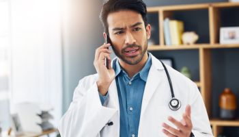 Confused doctor, man and phone call in hospital for communication, healthcare advice and life insurance. Question, medical employee and talking on smartphone for telehealth, mobile contact or problem