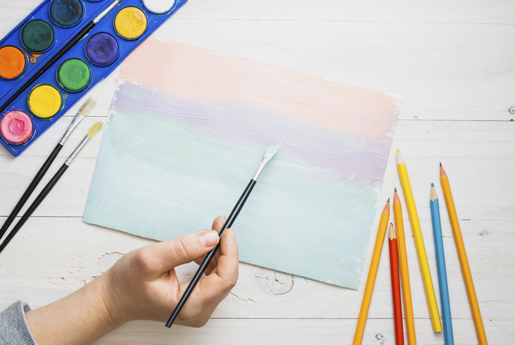 Person s hand painting paper with paint brush watercolor desk