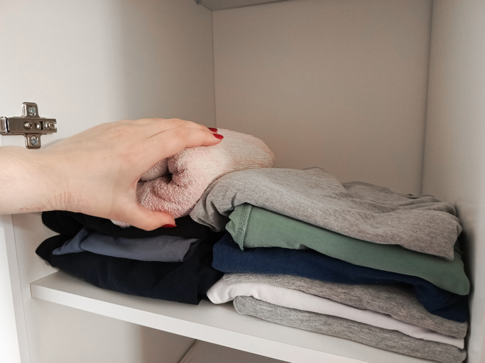 A woman's hand takes clothes from a stack of folded clothes. A stack of clothes on a shelf in the closet. Background, place for text.