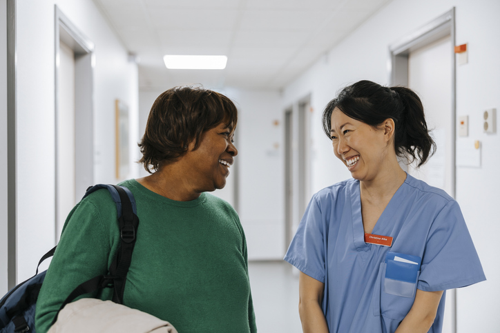 Happy senior woman talking with female nurse in hospital corridor